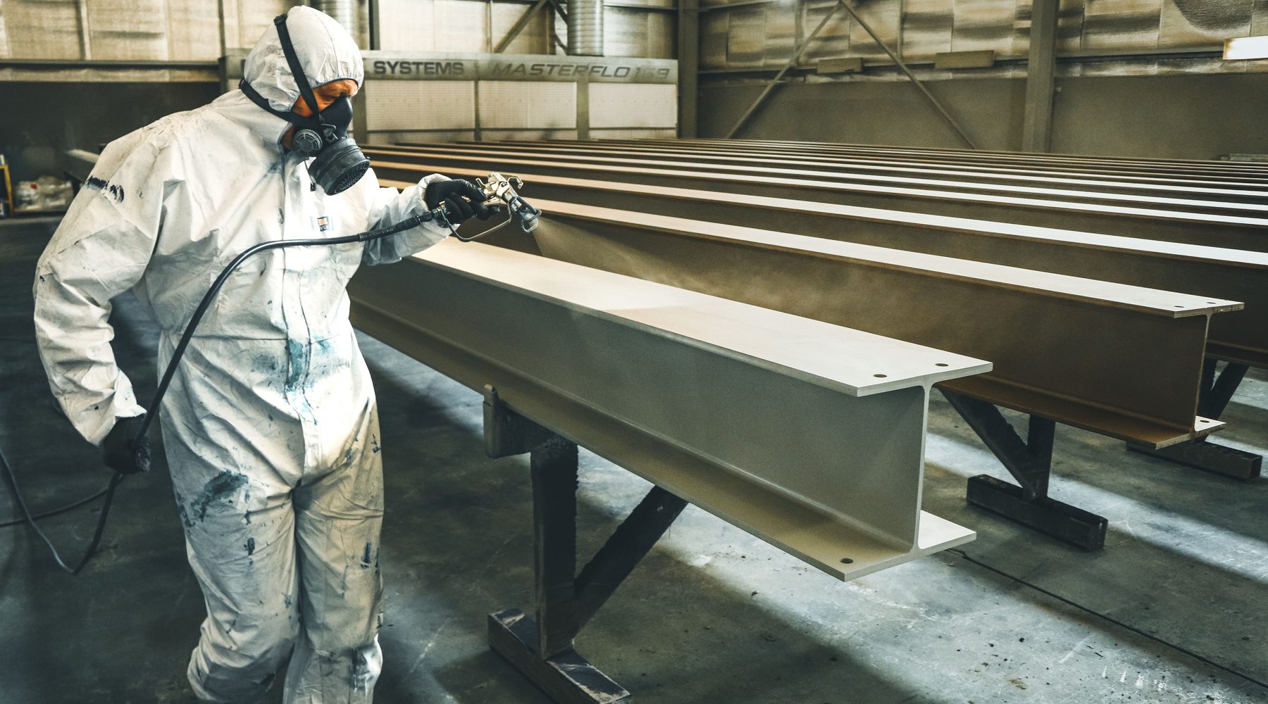 Worker spray coating structural steel in an industrial facility